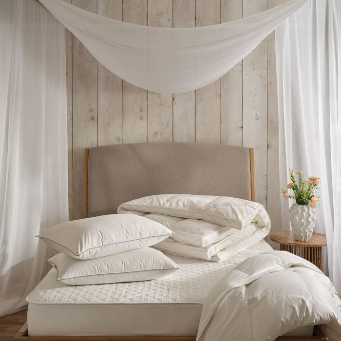 Down pillows, topper and duvet on a bed with a mattress protector. In a light and airy bedroom with net drapes. | Scooms