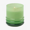The 7oz Stacked Glass Candle, crafted from green soy wax, glows in a glossy translucent green glass holder with a ribbed base, set against a plain white background.