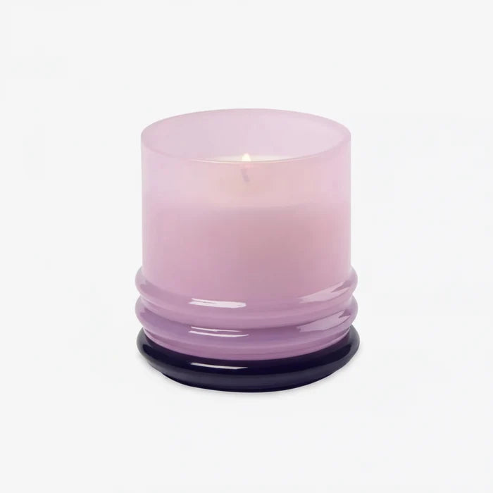 The 7oz Stacked Glass Candle features lit soy wax in a translucent light purple glass holder with a round, ridged base, displayed against a plain white background.