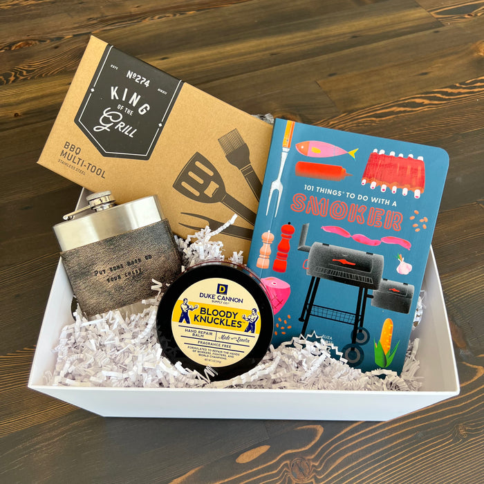 Craft the ideal present with Lit Decor and Gift’s Custom Gift Boxes, featuring a BBQ multi-tool, metal flask, Duke Cannon Bloody Knuckles balm, and “101 Things To Do With A Smoker,” all arranged in white shredded paper.