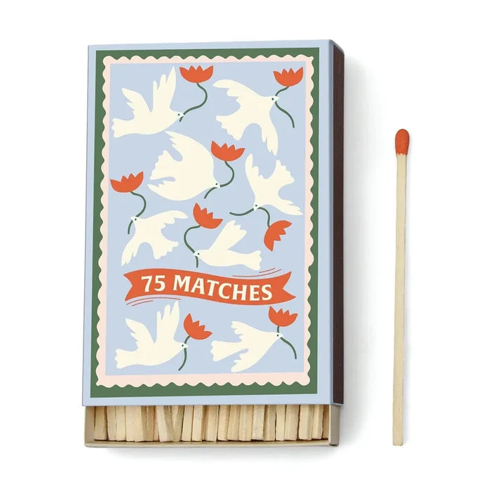 A Dopo 75ct Boxed Matches: a box of 75 safety matches with a decorative cover of white doves and red flowers on blue, reminiscent of Mediterranean travel. Includes one red-tipped match beside the box.