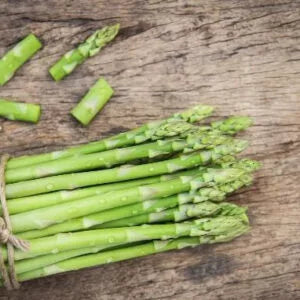 This is an image of green stems of Asparagus tied together with a rope kept against brown color black color background.