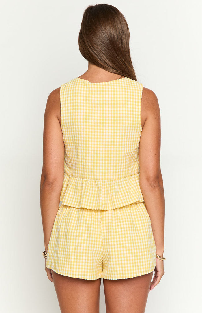 Rear view of a yellow gingham sleeveless top with a scalloped back neckline and a tiered peplum hem