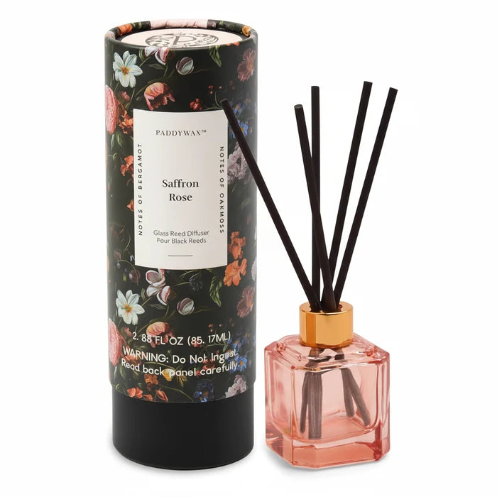 The Botanical Diffuser Set features a floral-patterned box beside a pink glass bottle with a gold collar and four black reeds, highlighting the Botanica Collection’s modern and luxurious scent experience.