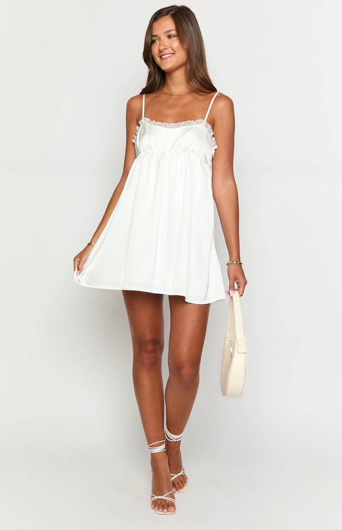 Front view of a white babydoll mini dress with delicate lace trim on the neckline and a flowy A-line skirt