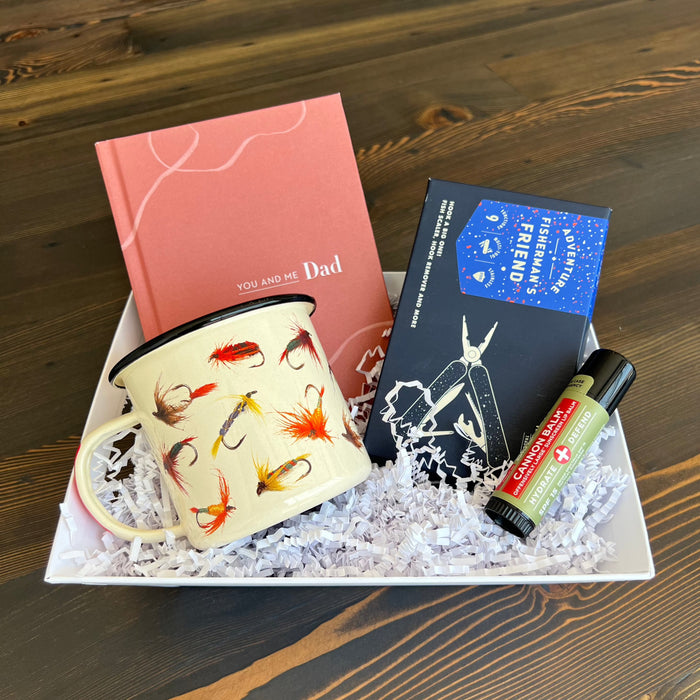 Craft the perfect gift with Lit Decor and Gift’s Custom Gift Boxes, featuring a pink “You and Me Dad” journal, fishing fly enamel mug, multi-tool, lip balm, and shredded filler—beautifully arranged on a wooden surface.