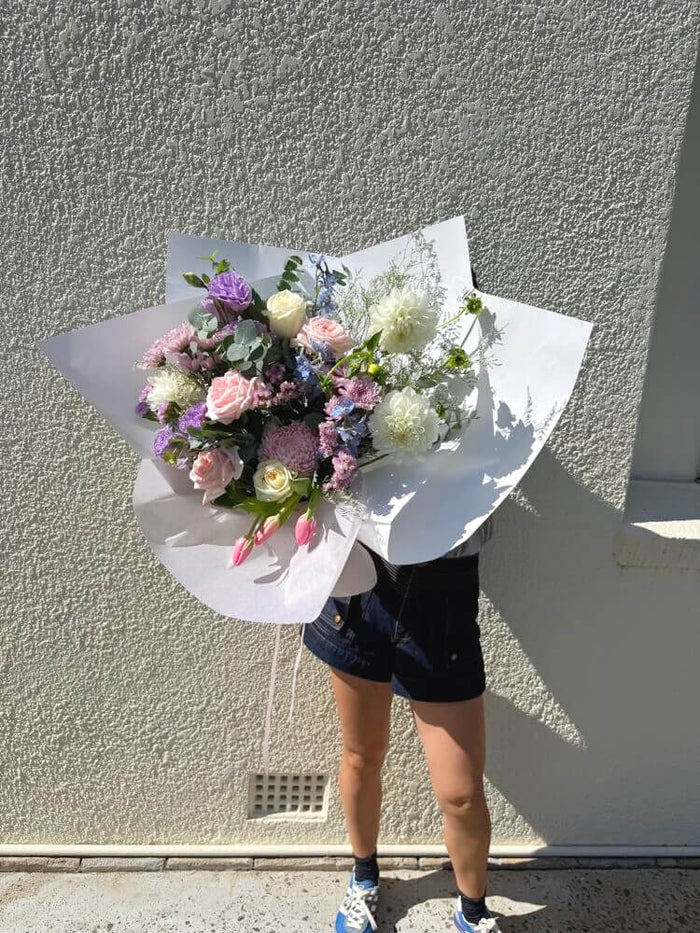 Person holding a bouquet of mothers day flowers in pastel colours against a gray wall