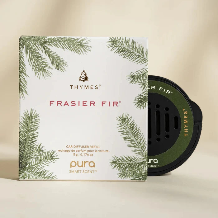 A Pura Car Diffuser Refill package with green fir branch illustrations and a round black car air freshener beside it, set against a light beige background—ideal for infusing your car with fresh, natural fragrance.
