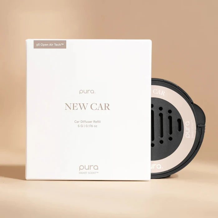 A white box labeled Pura Car Diffuser Refill sits next to a circular car air freshener refill with a sleek black and silver design, both displayed on a beige background.
