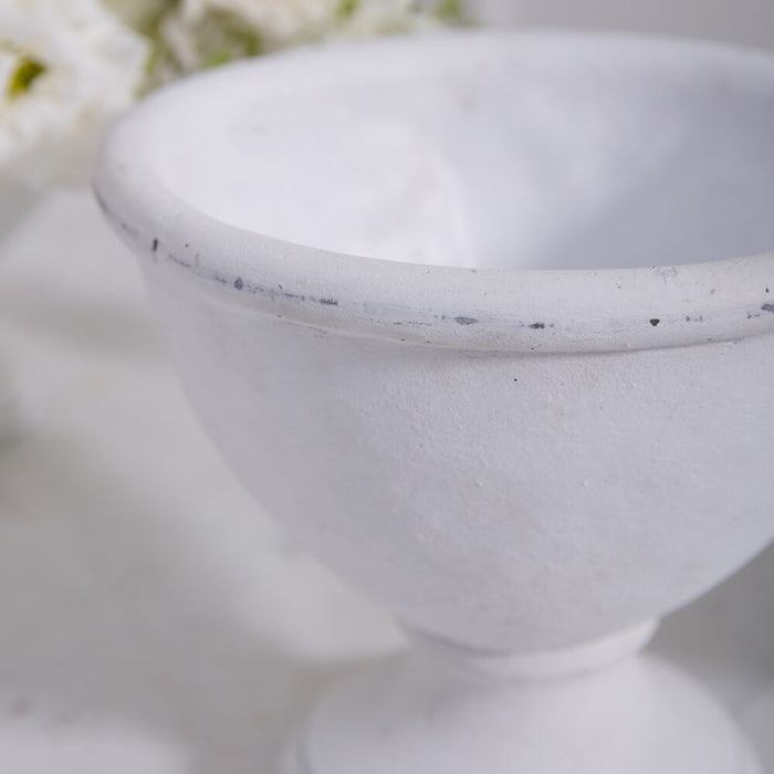 Close-up of the Rustic White Compote with a wide rim and pedestal base, ideal as a ceramic compote or floral arrangement vase. Blurred white flowers in the background enhance its serene, rustic charm.