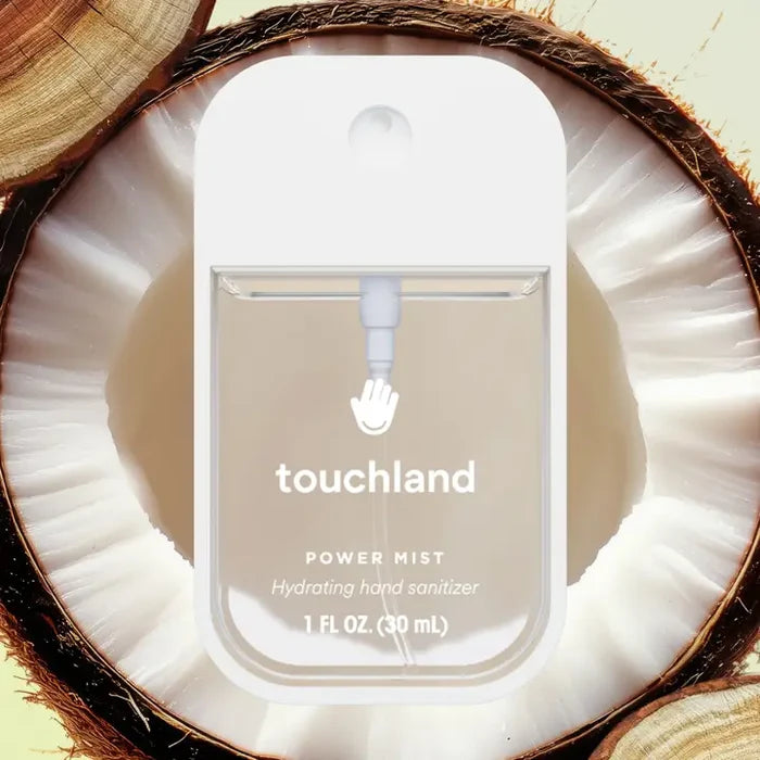 A bottle of Touchland Hand Sanitizer Mist sits on a halved coconut, highlighting its delicately scented, clear liquid against the coconut’s white interior and brown shell for irresistibly hydrated hands.