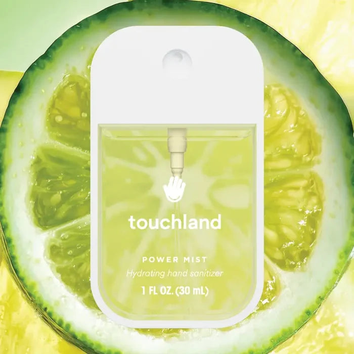 A bottle of Touchland Hand Sanitizer Mist, with yellow-green liquid inside, sits before a sliced lime. The clear label displays the name and 1 fl oz (30 mL) volume—ideal for delicately scented, hydrated hands.