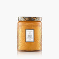 The Voluspa 18oz Glass Jar Candle features amber-colored embossed glass with floral patterns and a metallic lid, labeled "Voluspa Baltic Amber." Made from coconut wax, the candle is displayed against a white background.