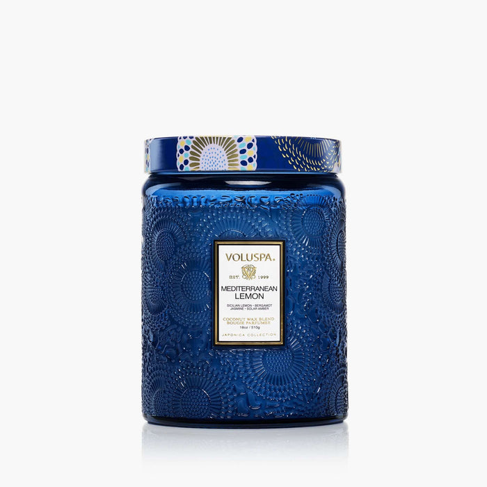 The Voluspa 18oz Glass Jar Candle features a large blue embossed design with a decorative lid, clean-burning coconut wax blend, hand-poured in the USA, and is part of the elegant Japonica Collection.